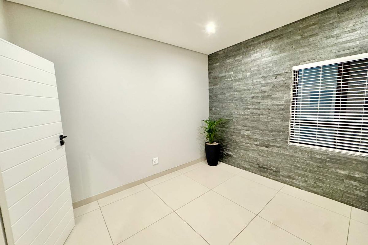 A bright, empty bedroom featuring a modern grey stone feature wall, large format floor tiles, and recessed lighting.