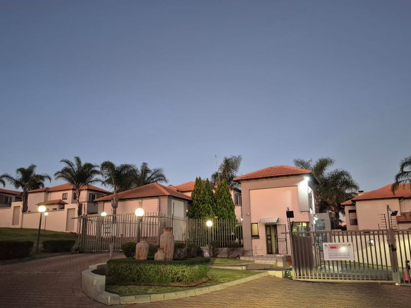 Front entrance view of the apartment complex featuring a paved driveway, secure gated access, and perimeter electric fencing.