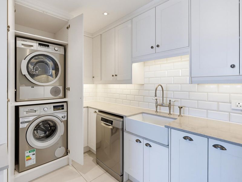A modern, well-appointed scullery featuring white cabinetry, subway tile backsplash, an apron sink, and integrated laundry appliances.