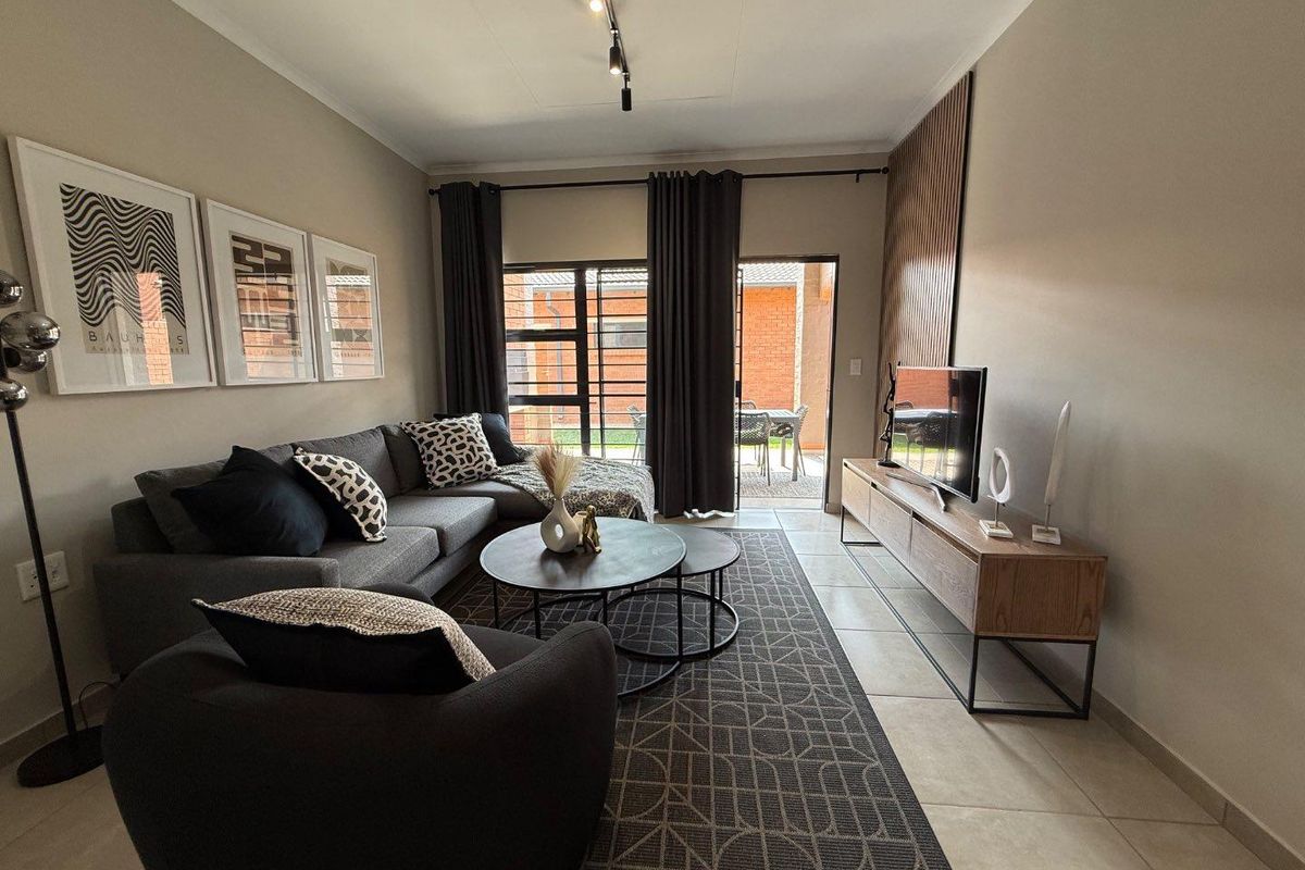 A modern living room featuring tiled flooring, track lighting, and a feature wall panel, with direct access to an outdoor patio area.
