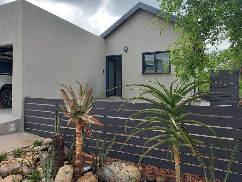 Front elevation of a modern home featuring neutral rendered walls, dark aluminium window frames, and a contemporary horizontal slat fence.