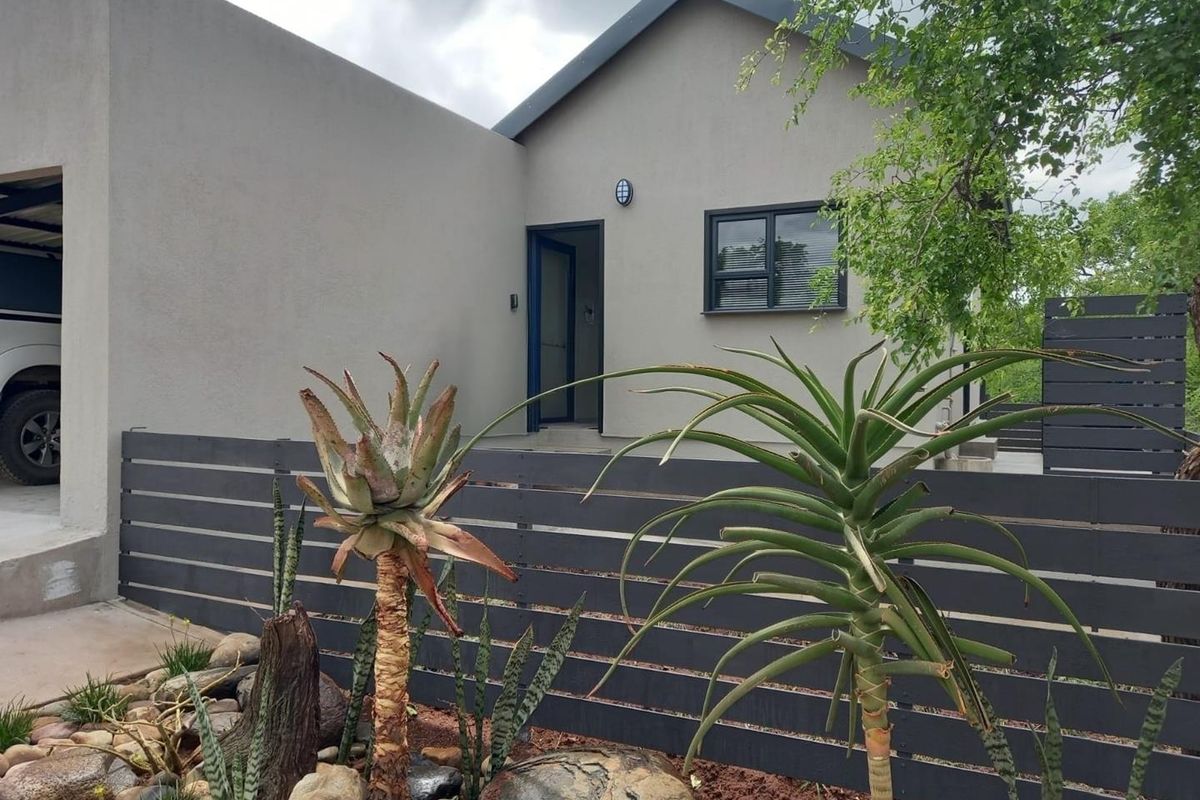 Front elevation of a modern home featuring neutral rendered walls, dark aluminium window frames, and a contemporary horizontal slat fence.