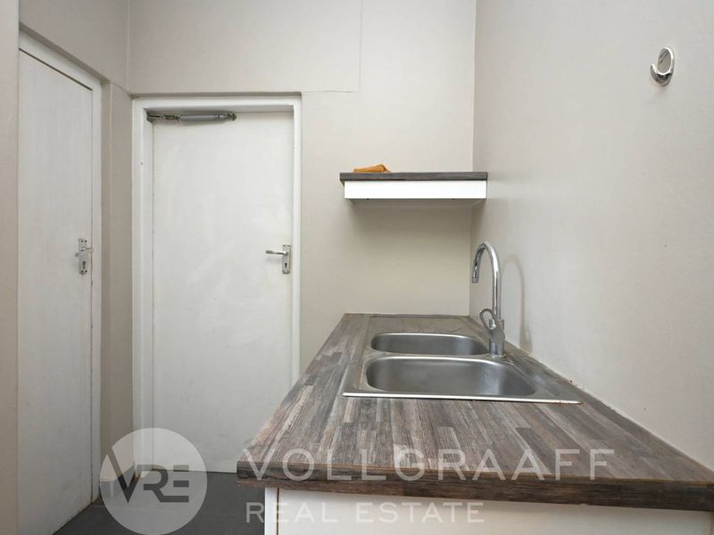 A functional scullery or utility area featuring a double bowl stainless steel sink, laminate countertop, and wall-mounted storage shelf.
