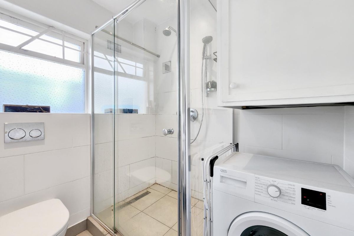 A clean, functional bathroom featuring a glass-enclosed shower, wall-mounted toilet, and integrated cabinetry with laundry facilities.