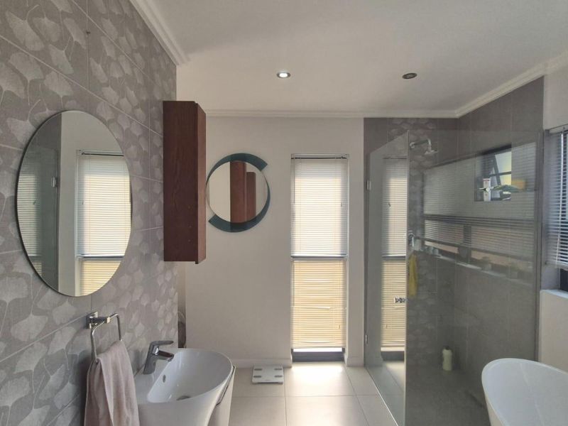 Modern bathroom featuring a freestanding bathtub, glass-enclosed shower, wall-mounted basin, and stylish patterned wall tiling with recessed lighting.