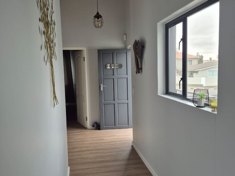 A bright, modern hallway featuring laminate flooring, exposed timber ceiling beams, and a neutral color palette, leading to a panelled interior door.