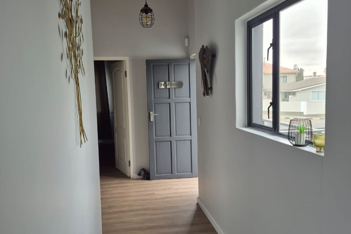 A bright, modern hallway featuring laminate flooring, exposed timber ceiling beams, and a neutral color palette, leading to a panelled interior door.