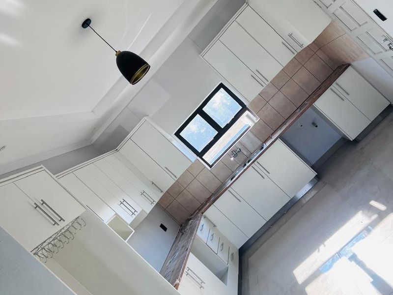 A modern, clean kitchen featuring white cabinetry, tiled backsplash, and ample counter space, presented in a bright, empty, and well-maintained condition.