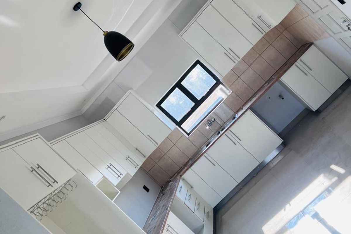 A modern, clean kitchen featuring white cabinetry, tiled backsplash, and ample counter space, presented in a bright, empty, and well-maintained condition.