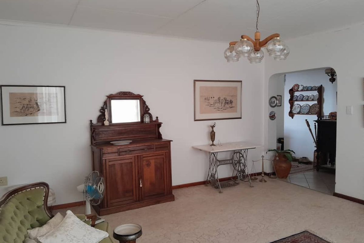 A spacious living room featuring neutral walls, carpeted flooring, and a classic chandelier, with an arched doorway leading to an adjacent area.