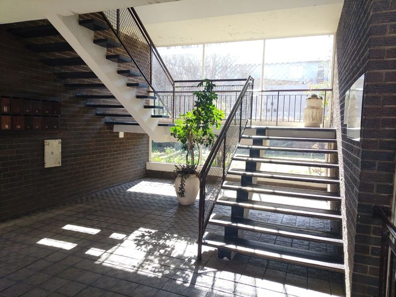 A spacious entrance foyer featuring a central staircase, brick wall finishes, and large windows providing natural light.