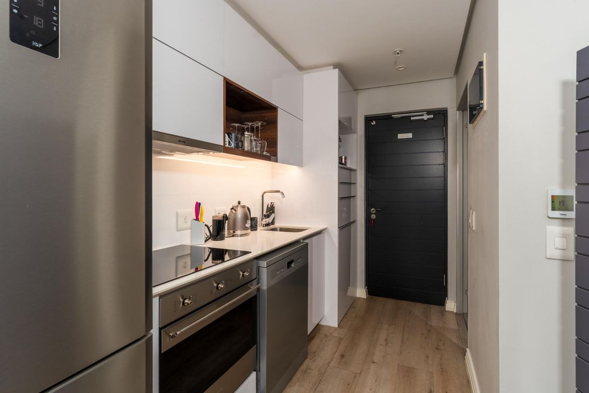 Modern compact kitchen featuring sleek white cabinetry, integrated appliances, electric hob, oven, and high-quality laminate flooring in a well-lit, efficient layout.