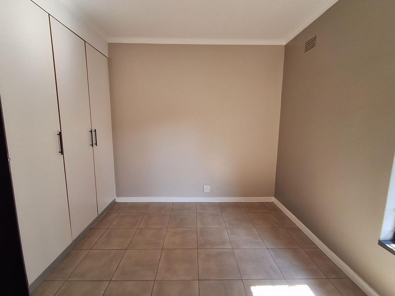 A clean, empty bedroom featuring neutral-toned walls, tiled flooring, and ample built-in cupboard storage.