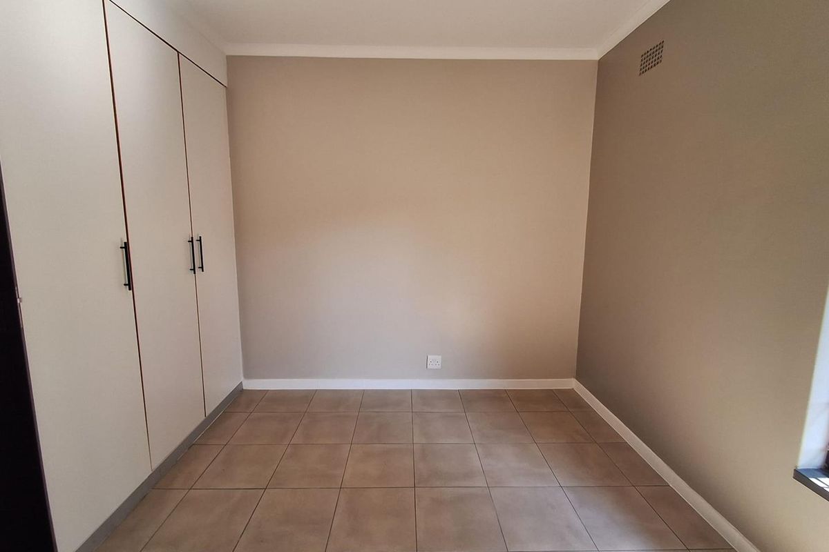 A clean, empty bedroom featuring neutral-toned walls, tiled flooring, and ample built-in cupboard storage.
