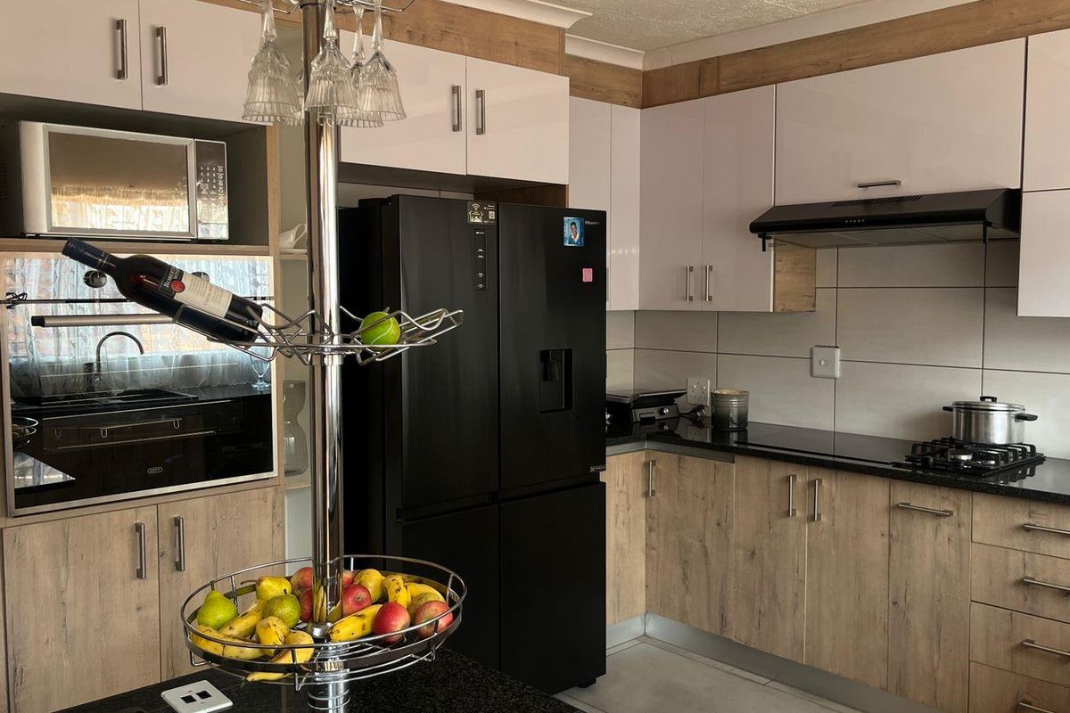 Modern kitchen featuring wood-grain cabinetry, black granite countertops, built-in oven, microwave housing, and a sleek extractor fan.