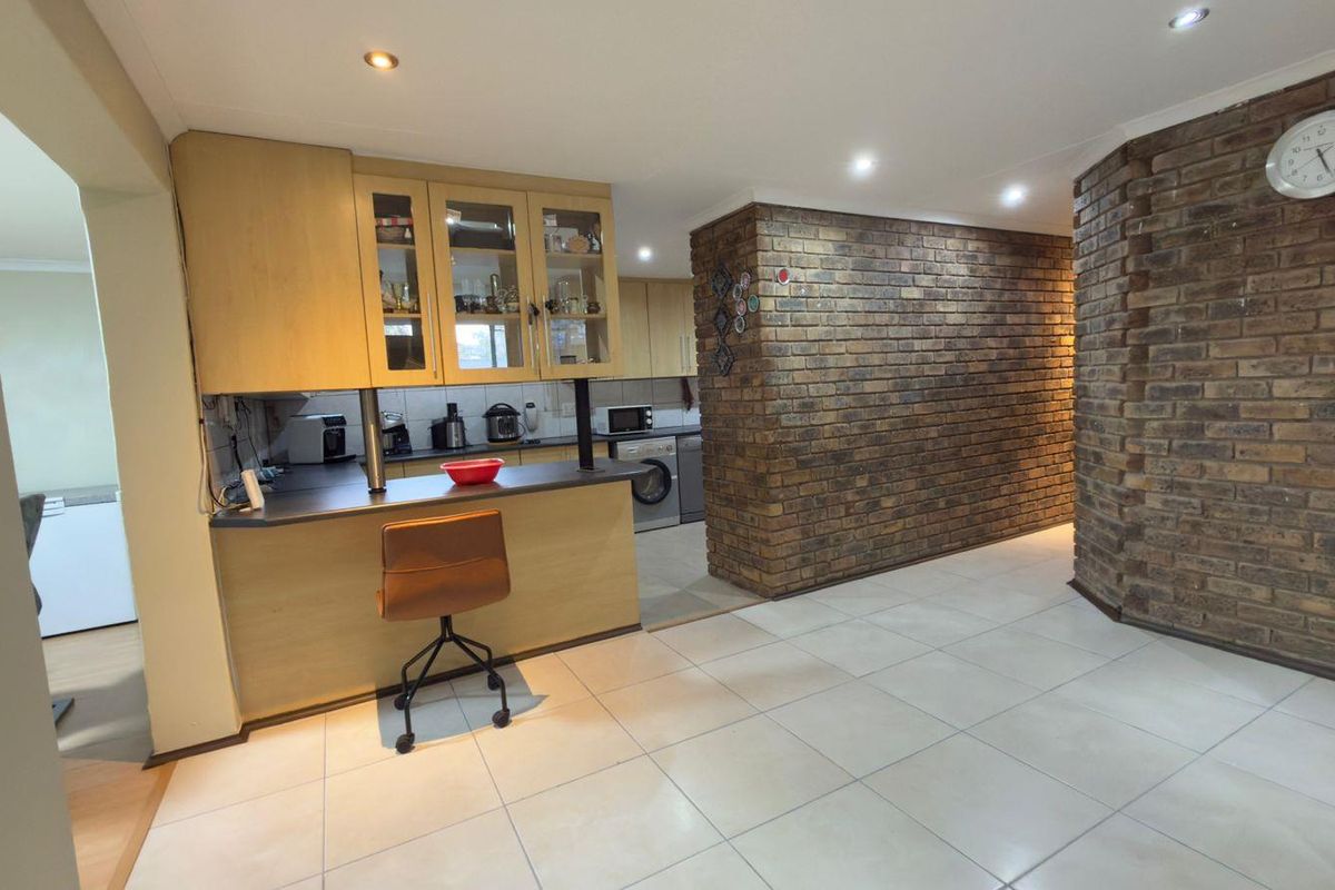 A functional kitchen featuring light wood cabinetry, laminate countertops, and a distinctive exposed brick feature wall, complemented by modern recessed lighting and tiled floors.
