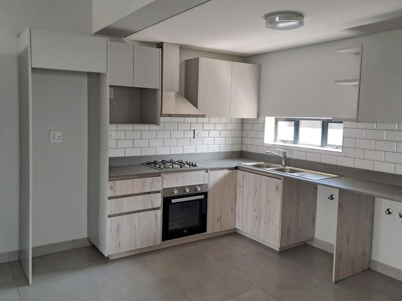 A modern, clean kitchen featuring light wood-finish cabinetry, stone countertops, a gas hob, electric oven, and a classic subway tile backsplash.