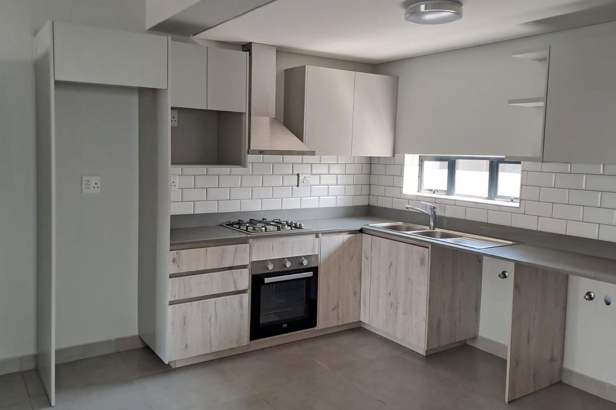 A modern, clean kitchen featuring light wood-finish cabinetry, stone countertops, a gas hob, electric oven, and a classic subway tile backsplash.
