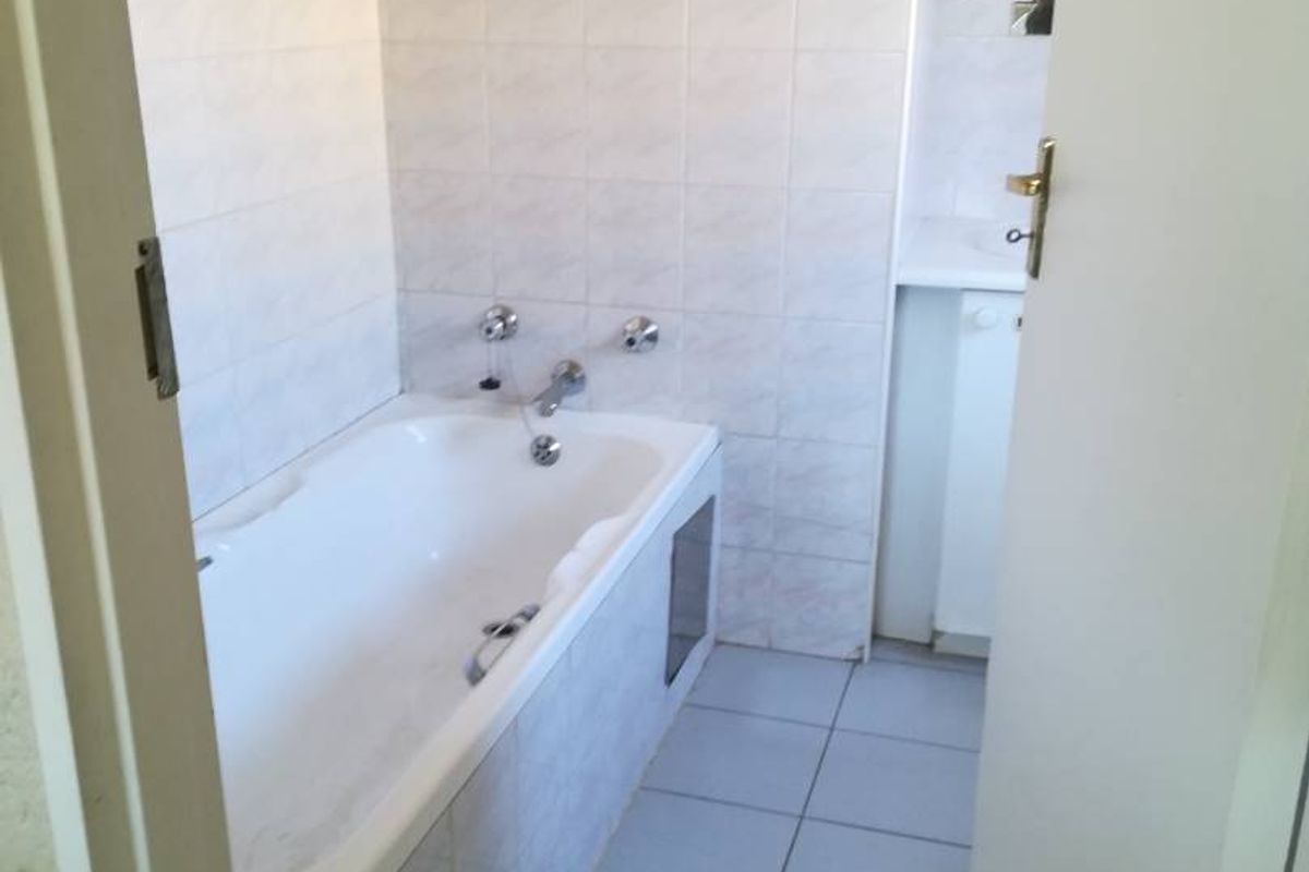 A functional bathroom featuring a built-in bathtub with tiled surround and ceramic flooring, presenting a dated aesthetic in need of modernization.