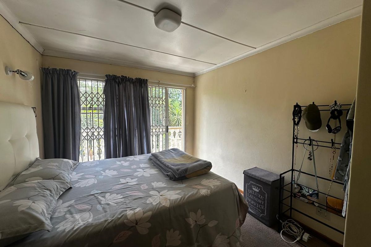 A bedroom featuring a sliding door with a security gate, providing access to an outdoor area, with standard ceiling lighting and neutral wall finishes.