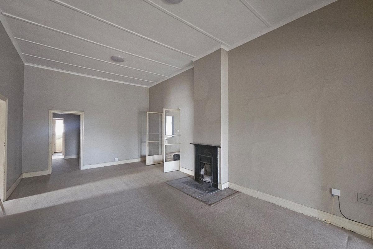 Spacious living room featuring a traditional fireplace, neutral wall finishes, and carpeted flooring, offering a blank canvas for renovation.