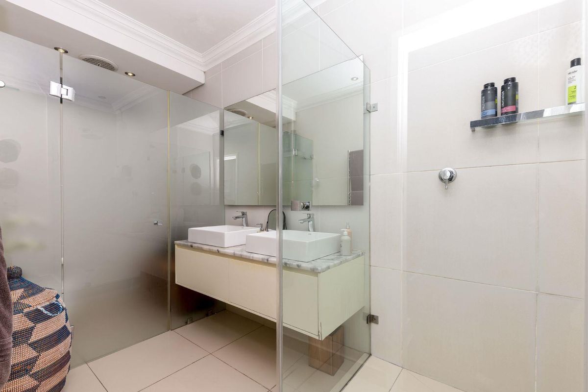 Modern bathroom featuring a double vanity with vessel sinks, marble countertop, wall-mounted cabinetry, and a spacious frameless glass shower enclosure.