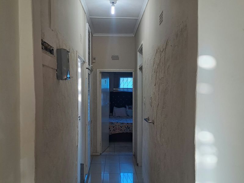 A narrow hallway featuring tiled flooring and louvered doors, requiring cosmetic wall repairs to improve the overall finish.