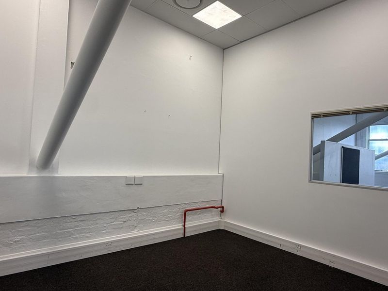 A clean, empty office space featuring neutral white walls, dark carpeting, an internal window, and exposed structural elements, suitable for a professional workspace.