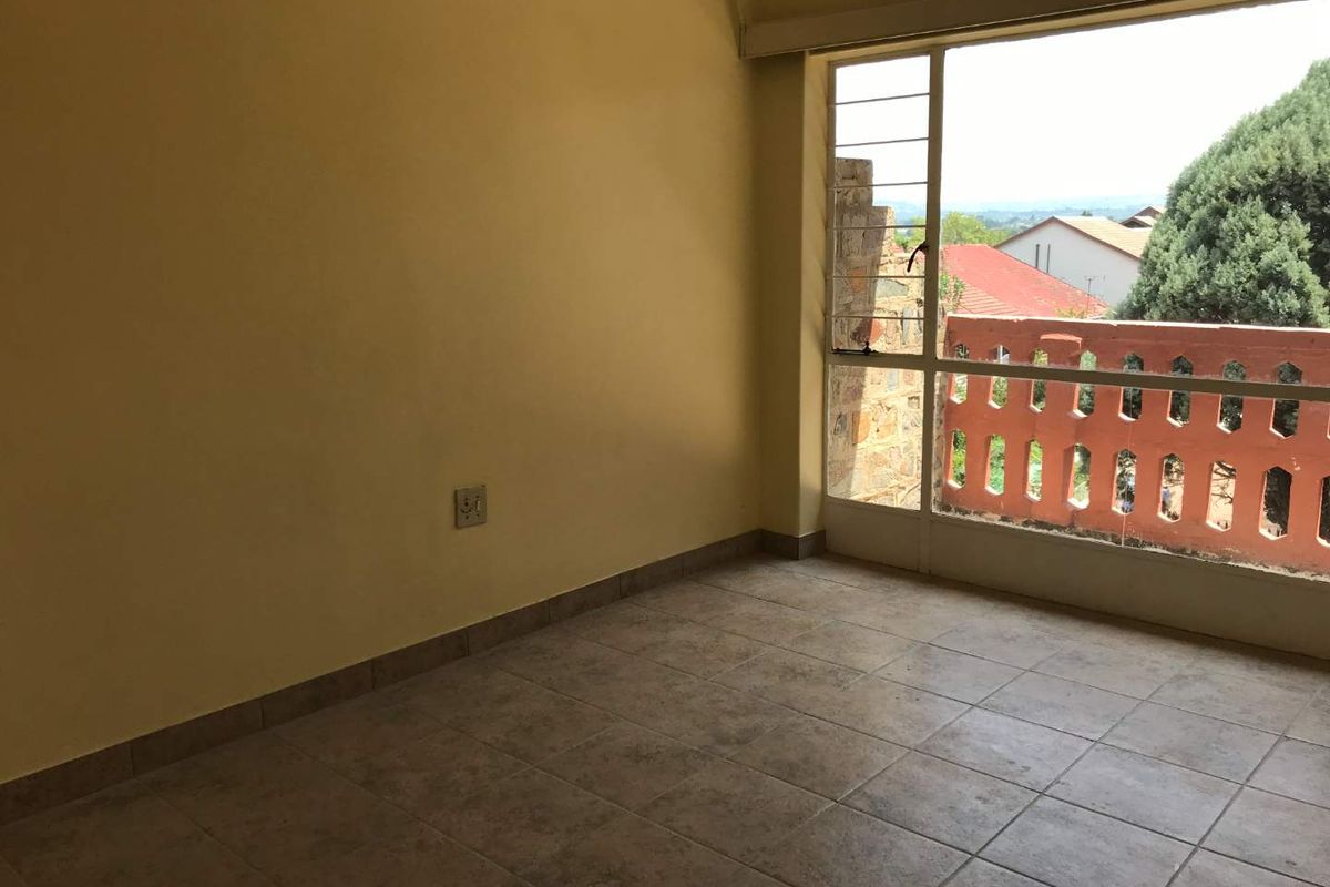 An empty bedroom featuring tiled flooring, a large window with natural light, and access to an outdoor balcony area.