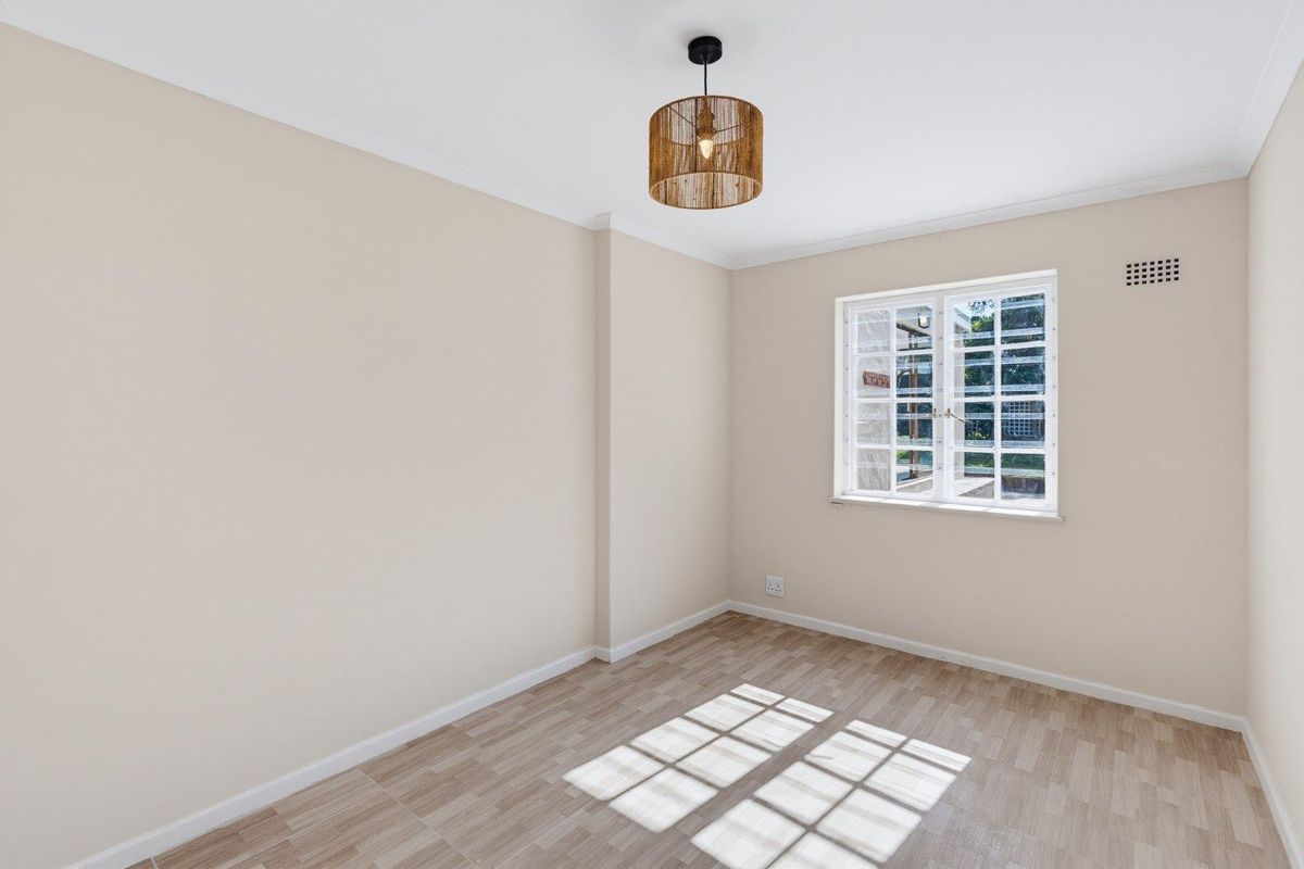 A bright, empty bedroom featuring neutral walls, laminate flooring, and a window with security bars, offering a clean and versatile space.