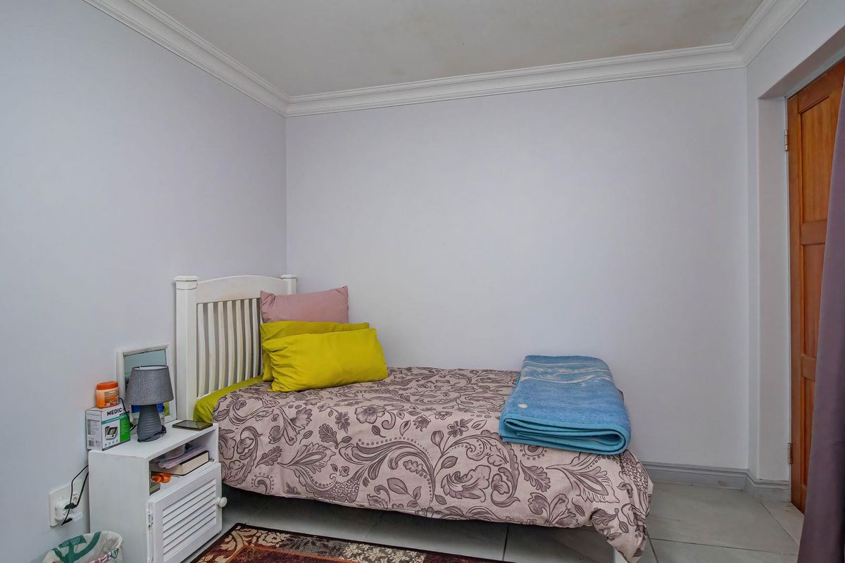 A simple bedroom featuring tiled flooring, crown molding, and a wooden door, with visible ceiling staining requiring attention.