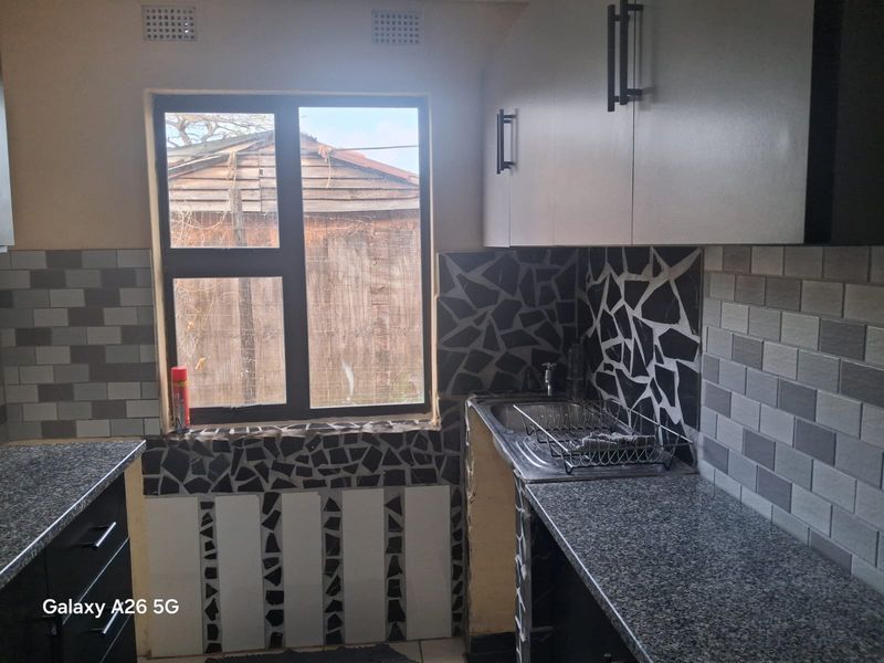 Compact kitchen featuring granite countertops, built-in cabinetry, and a stainless steel sink, currently requiring finishing touches to the tiling and cabinetry base.