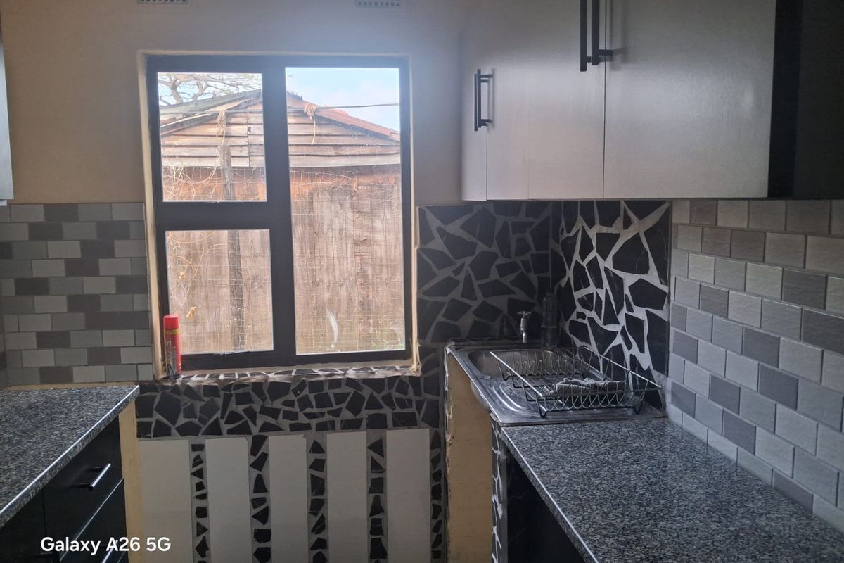 Compact kitchen featuring granite countertops, built-in cabinetry, and a stainless steel sink, currently requiring finishing touches to the tiling and cabinetry base.