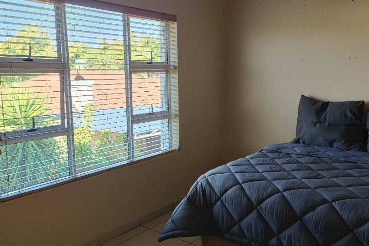 A bedroom featuring tiled flooring, neutral wall tones, and large windows fitted with venetian blinds, offering a clean and functional living space.