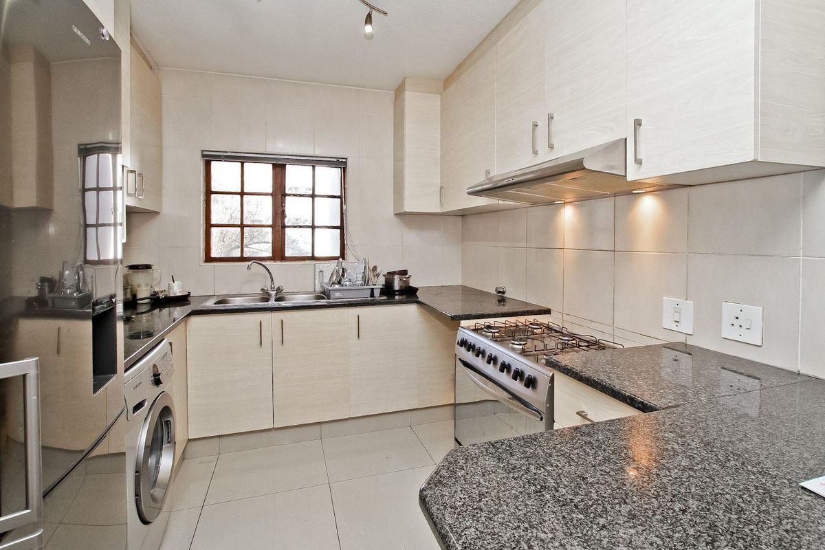 A functional kitchen featuring light wood-finish cabinetry, granite countertops, a stainless steel gas stove with extractor fan, and tiled flooring.