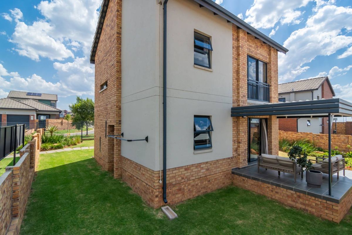 Rear view of a modern two-story brick house featuring a covered patio, balcony, and well-maintained garden area.
