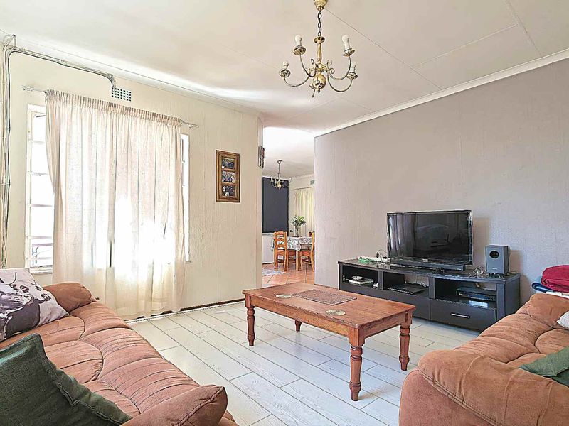A living room featuring tiled flooring, a central chandelier, and an open-plan layout leading to the dining area.