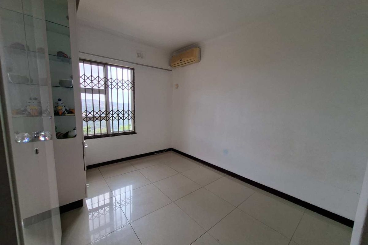A bedroom featuring tiled flooring, a built-in display cabinet, and a wall-mounted air conditioning unit with security bars on the window.