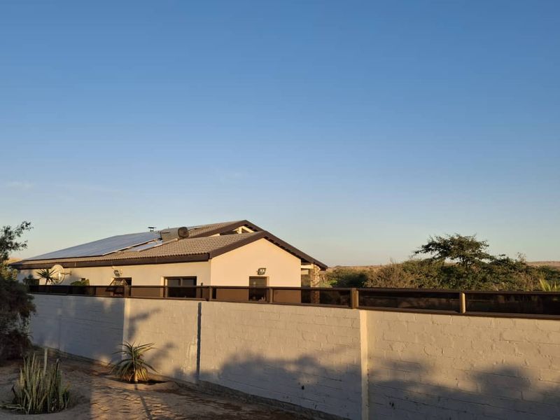 Rear view of the property featuring a tiled roof with installed solar panels and a solar geyser, enclosed by a secure boundary wall.
