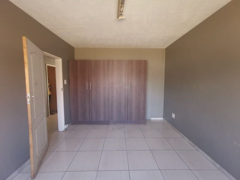 A spacious, empty bedroom featuring neutral tiled flooring and built-in wooden cupboards, offering a blank canvas for personalization.