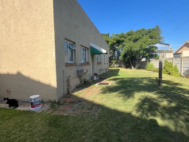 Rear exterior view of the apartment featuring a lawn, brick pathway, external wash basin, and boundary walling.