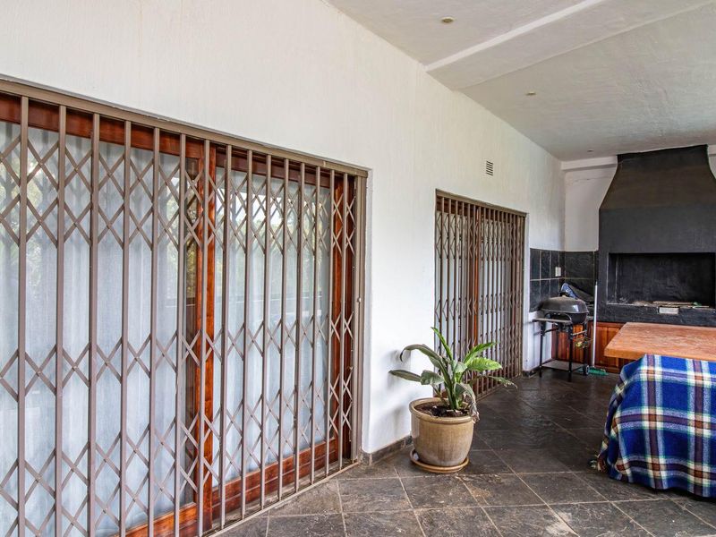 Covered patio featuring a built-in braai, dark tiled flooring, and secure sliding door access to the interior living spaces.