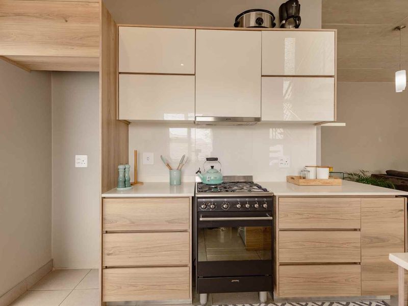 Modern kitchen featuring light wood-grain cabinetry, high-gloss upper cabinets, stone countertops, and a built-in gas stove with an extractor fan.