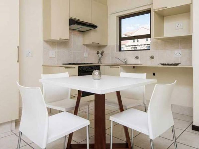 Open-plan kitchen and dining area featuring neutral built-in cabinetry, tiled flooring, and integrated cooking appliances.