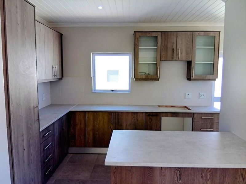 A functional kitchen space featuring wood-finish cabinetry, light-toned countertops, and tiled flooring, currently awaiting the installation of a cooktop or stove.