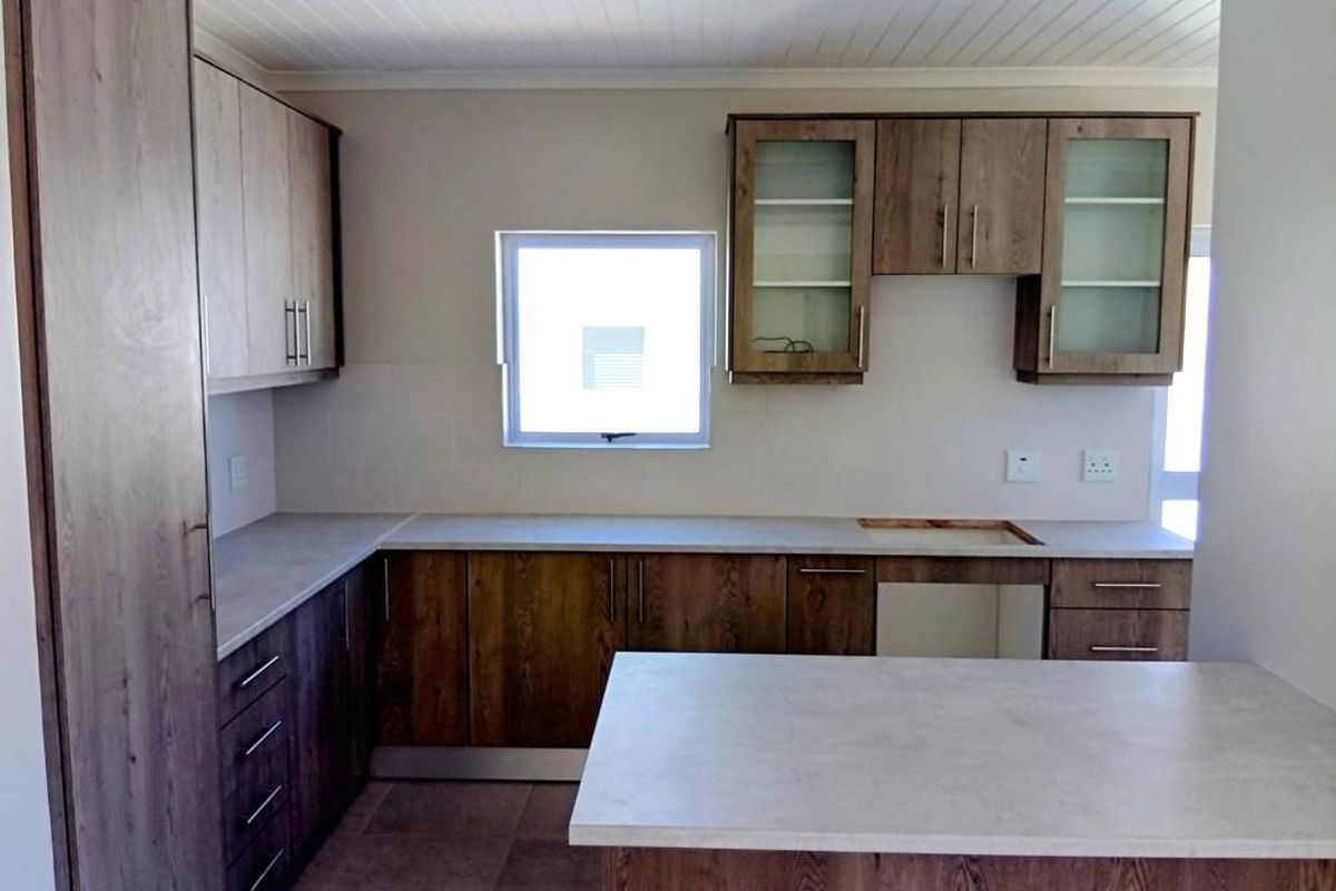 A functional kitchen space featuring wood-finish cabinetry, light-toned countertops, and tiled flooring, currently awaiting the installation of a cooktop or stove.