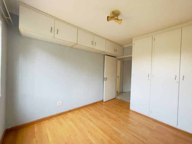 A vacant bedroom featuring laminate flooring, extensive built-in cupboard storage, and overhead cabinetry, offering a clean and functional space ready for personalization.