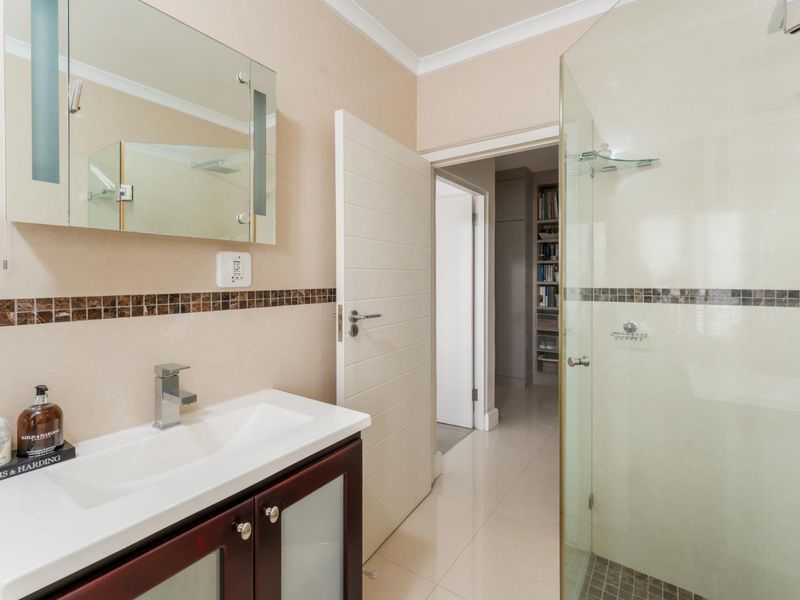 A well-maintained bathroom featuring a modern vanity cabinet, integrated sink, and a glass-enclosed shower with neutral wall tiles and mosaic accents.