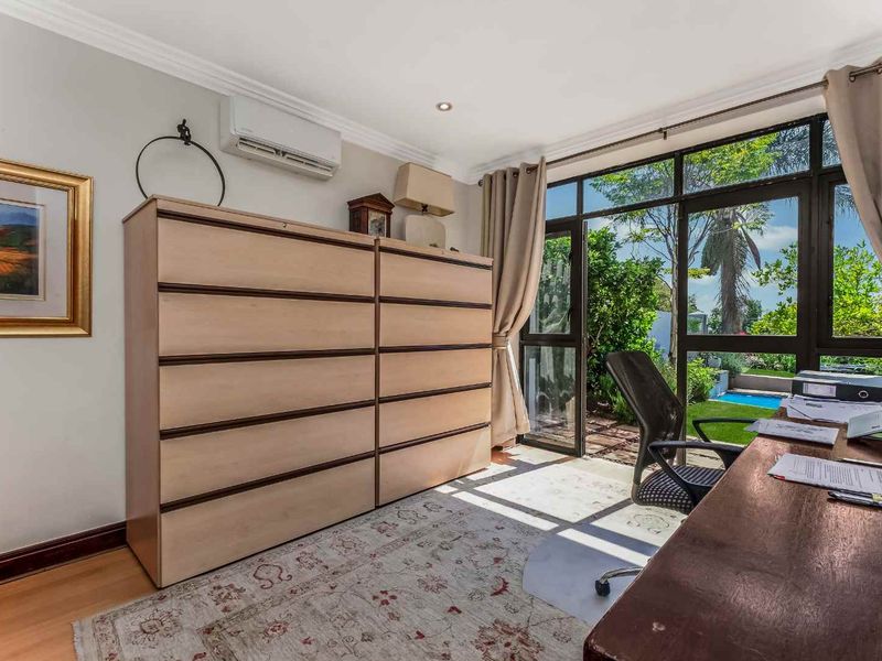 A bright home office featuring laminate flooring, a wall-mounted air conditioning unit, and large glass doors providing direct access to the garden.