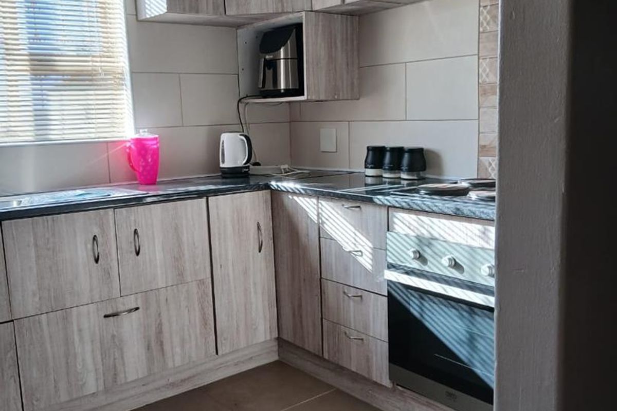A functional kitchen featuring light wood-grain laminate cabinetry, built-in oven, extractor fan, tiled backsplash, and neutral floor tiles.